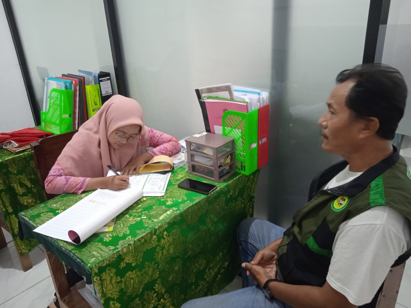 Seorang relawan yayasan berbincang dengan petugas yang mencatat informasi di meja.